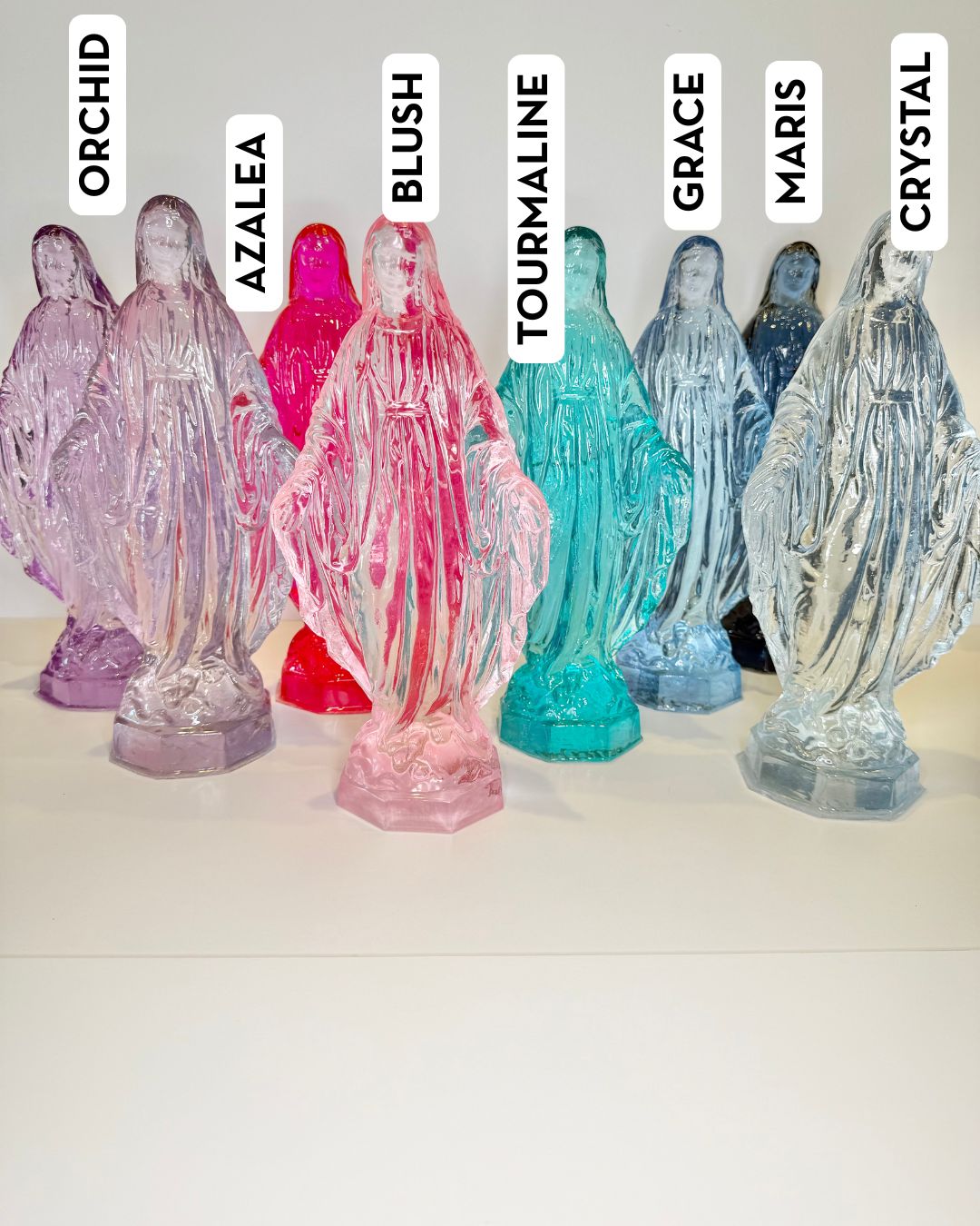 Eight translucent glass Virgin Mary statues in various colors labeled with names