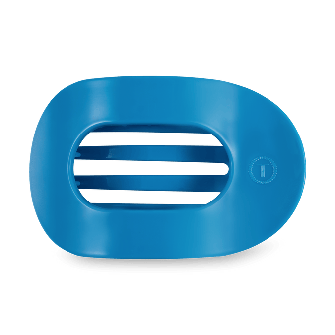 Studio shot of a matte blue oval object featuring four horizontal central slits and a small embossed circular logo with a letter T on the right, presented against a dark green background