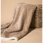 Photograph of a beige ribbed blanket with a white sherpa lining draped over a rustic wicker basket