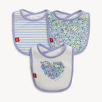 Product photography of three baby bibs including one with blue and white stripes, another with a small multicolored floral pattern, and a white bib featuring a floral heart design with Magnetic Me text, all edged with lilac trim and a red m logo tag