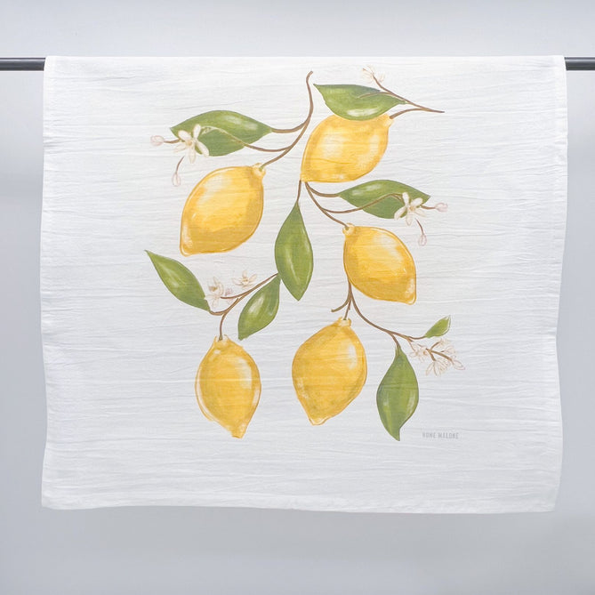 Printed fabric art by HOME MALONE featuring an illustration of lemon branches on a white kitchen towel with six bright yellow lemons fresh green leaves and small white blossoms