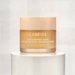 Product photography of Laneige Vanilla Lip Sleeping Mask in a frosted amber glass jar with a peach-toned lid and white text, displayed on a minimalist white cylindrical pedestal with a subtle reflection