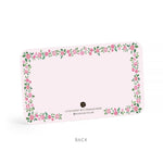 Paper note card by E. Frances Paper, the back of a light pink note card features a charming floral border of scattered pink flowers and green leaves along with the text LITTLE NOTES® BY E. FRANCES PAPER and an E.F. logo with a smiling face