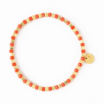Beaded bracelet with alternating coral red faceted beads and irregular gold beads featuring a small round gold logo charm on a white background