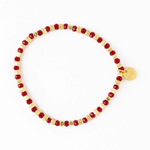 A red and gold bracelet featuring alternating faceted red crystal beads and hammered gold spacer beads with a small round gold charm