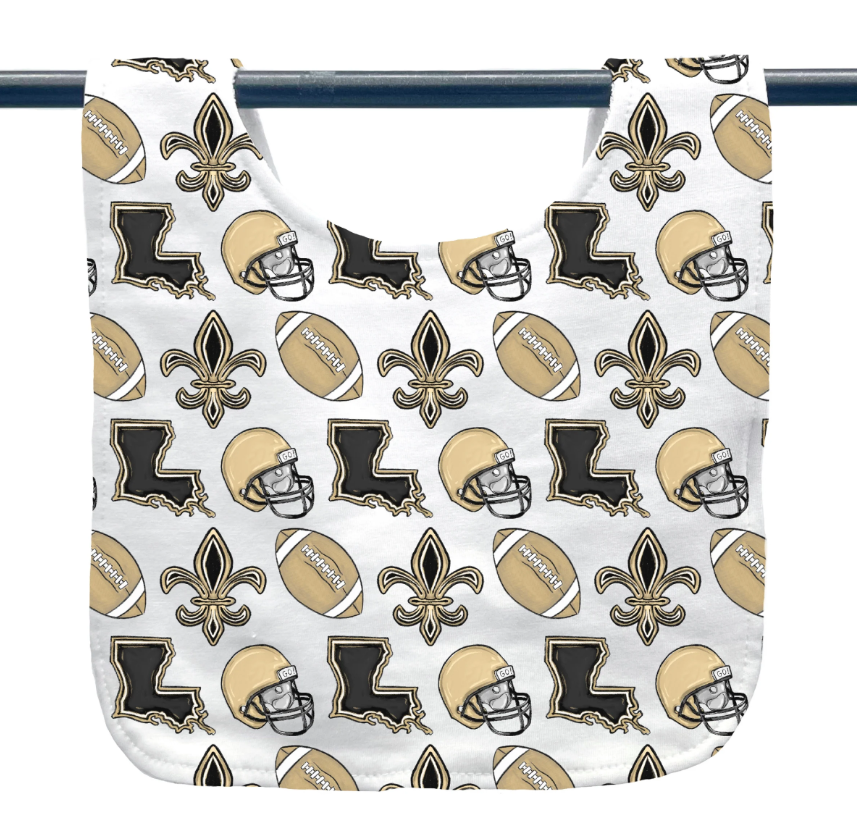Fabric baby bib featuring a repeating New Orleans Saints sports theme with iconic gold fleurs-de-lis, black Louisiana state outlines, gold football helmets, and brown footballs on a white background hanging from a rod