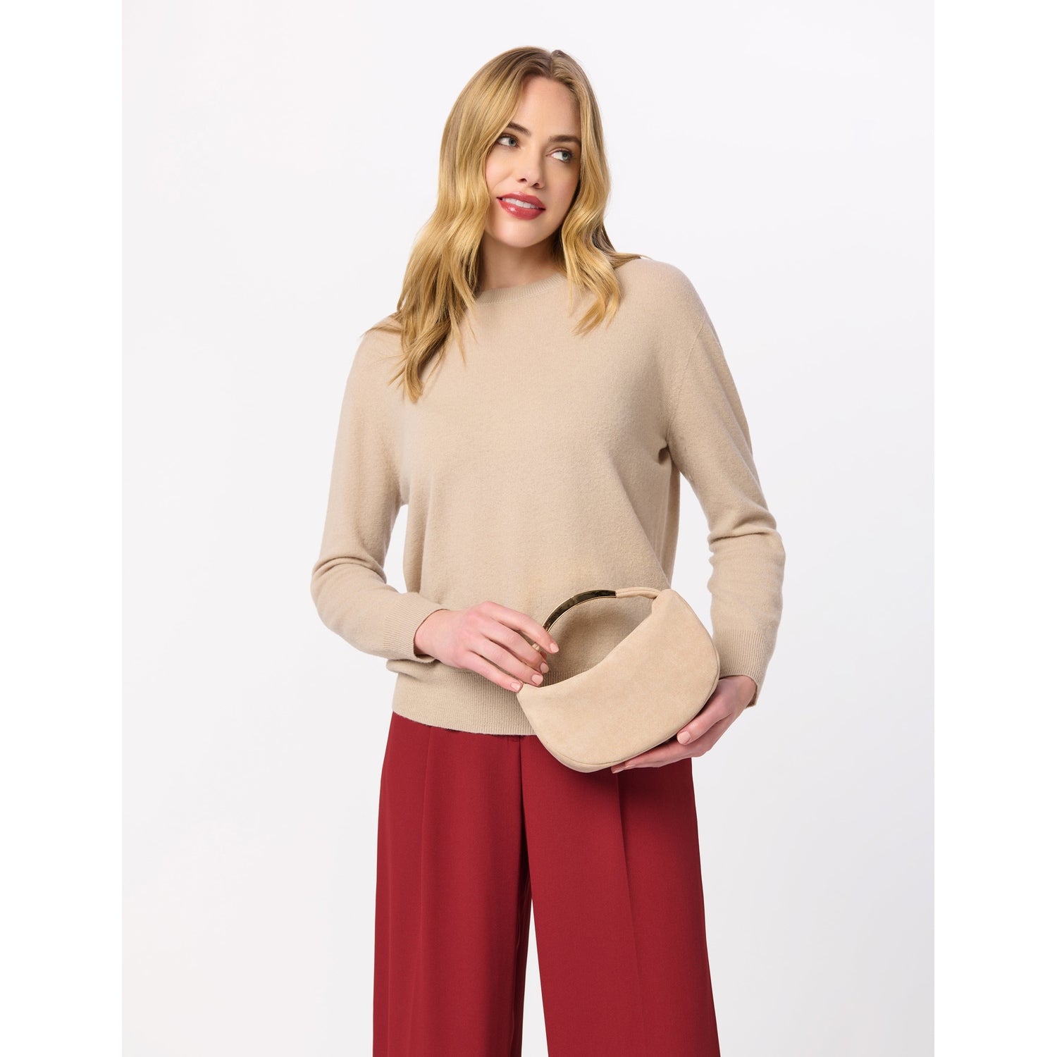 Woman wearing a beige sweater and red trousers holding a small beige handbag with a gold handle