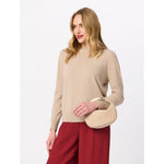 Woman wearing a beige crew neck sweater and red trousers holding a small beige handbag with a gold handle