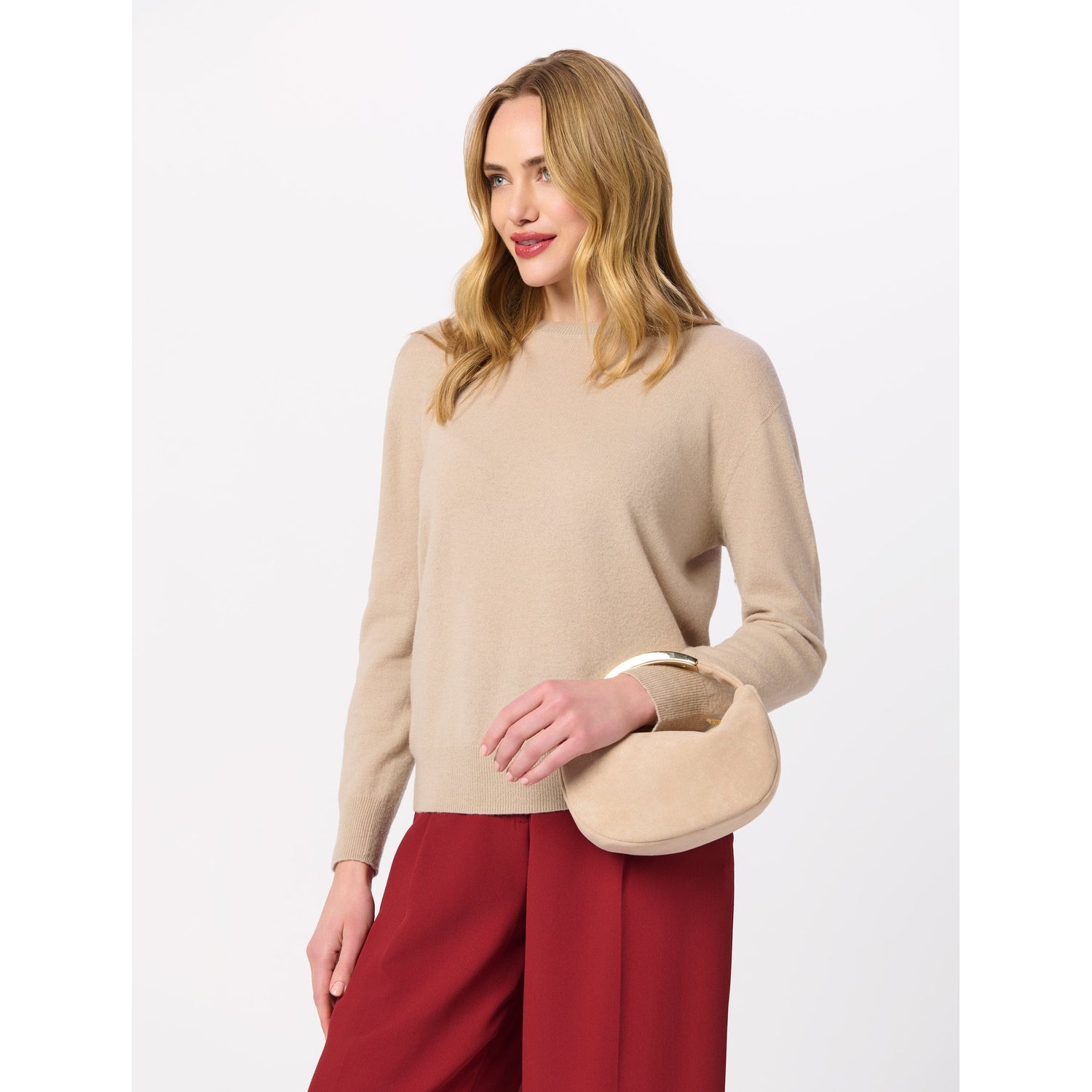 Woman wearing a beige crew neck sweater and red trousers holding a small beige handbag with a gold handle