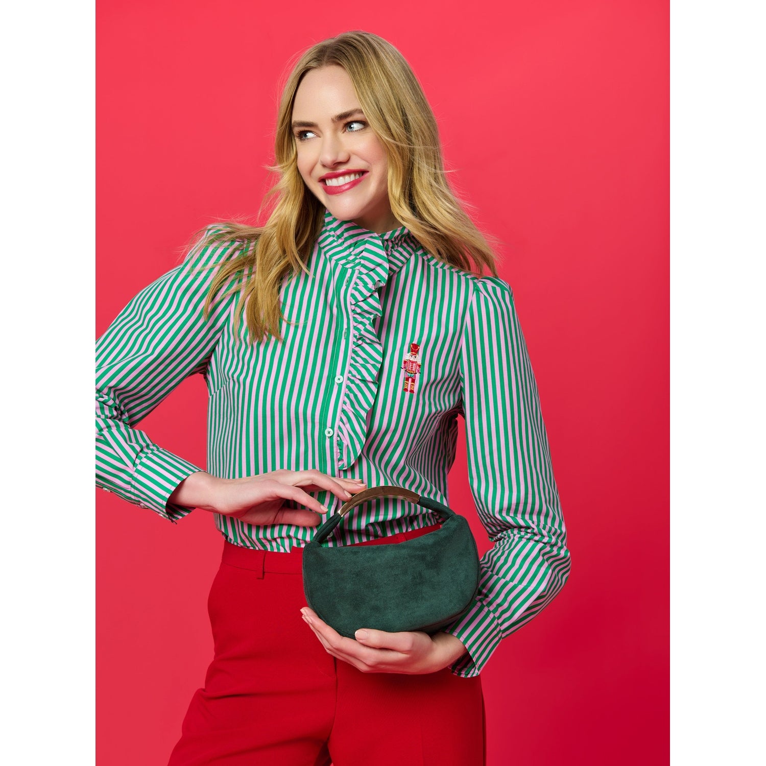 Woman wearing a green and pink striped ruffled blouse with a nutcracker embroidery and holding a dark green suede bag