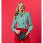 Woman wearing a green and pink striped ruffled shirt with a nutcracker embroidery and red trousers holding a green bag