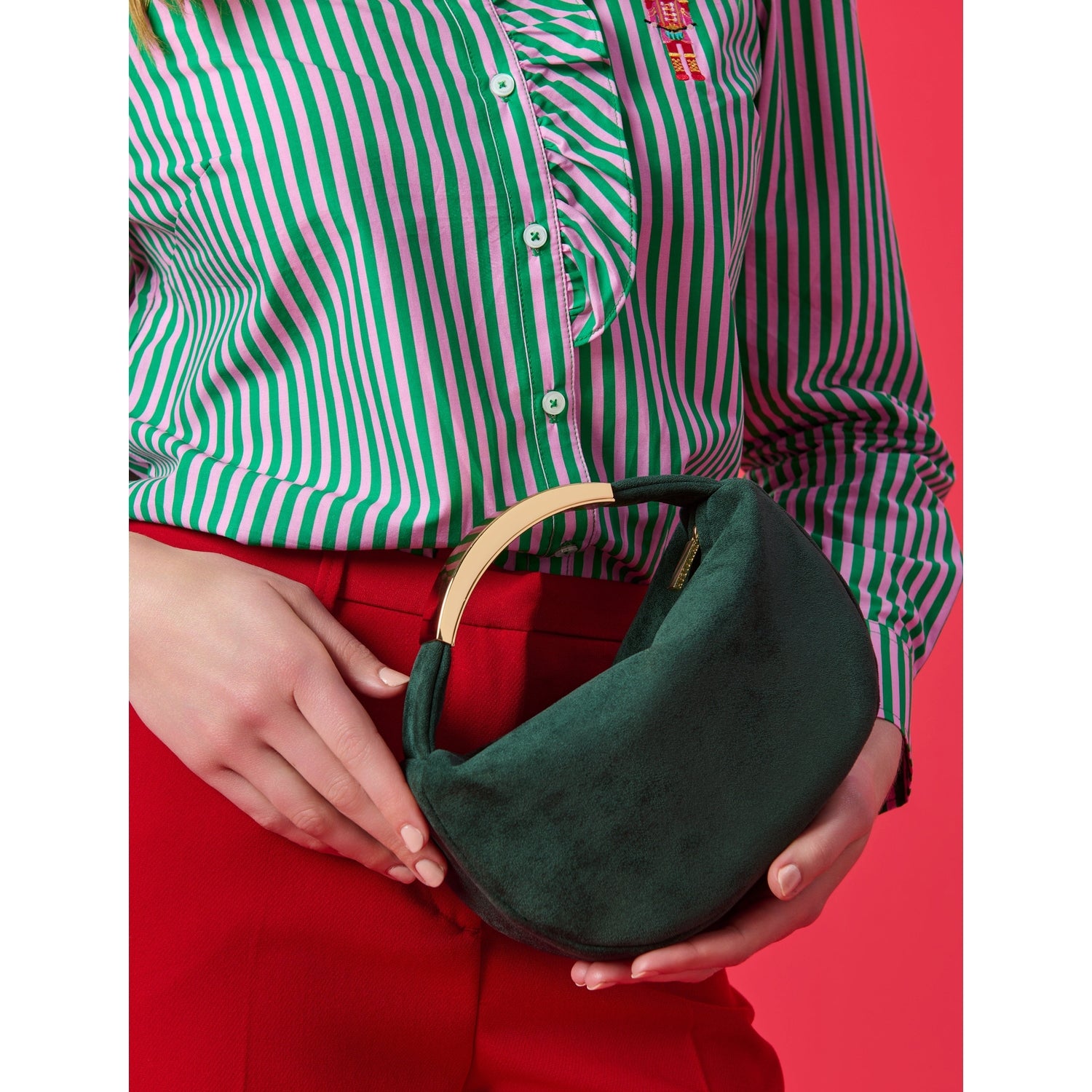Person holding a dark green suede handbag with a gold metal handle wearing a pink and green striped shirt