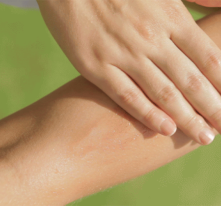 A hand gently massaging a forearm with smooth, hydrated skin that glistens, presented against a vibrant green background