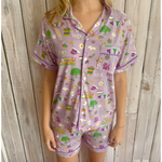 Photograph of a person wearing lavender short-sleeved pajamas with purple piping featuring colorful Mardi Gras masks, King Cakes, live oak trees, streetcars, and NOLA text