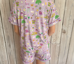 Light purple fabric print pajamas worn by a person from the back, adorned with a vibrant New Orleans pattern showcasing the Superdome, Bourbon Street lanterns, Mardi Gras beads, and king cake