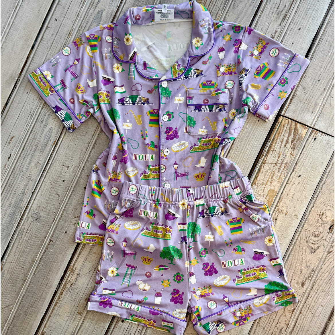 Lavender pajama set with a vibrant New Orleans Mardi Gras print showcasing NOLA text, iconic streetcars, and festive masks and beads