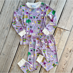 NOLA MERCANTILE children's pajama set depicting New Orleans culture and landmarks including the Superdome, Bourbon Street sign, Mardi Gras masks, and beignets in vibrant purple, green, and gold