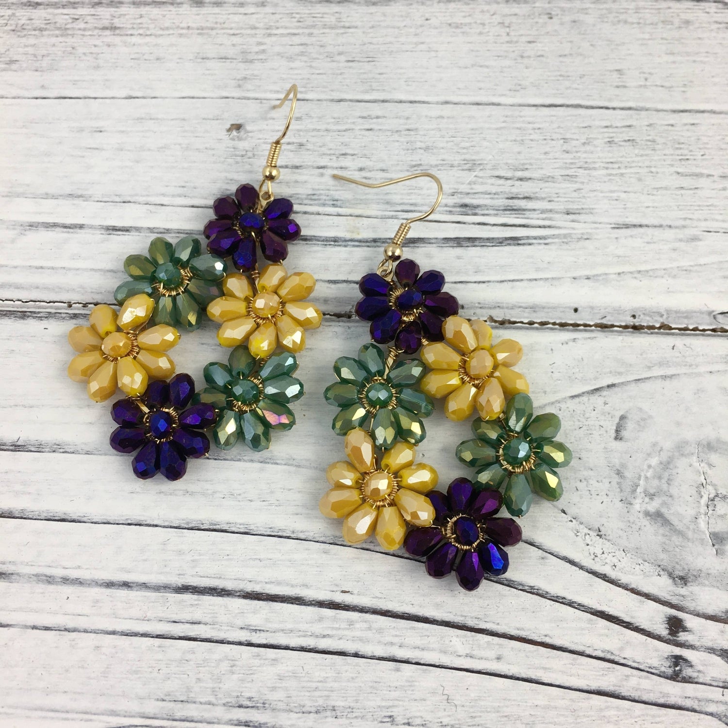 Handmade beaded earrings a pair of vibrant flower-shaped earrings crafted with faceted purple yellow and green glass beads and gold-toned hooks presented on a white distressed wooden surface