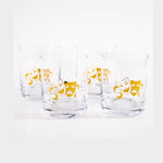 Glassware A set of four clear glass tumblers each featuring a vibrant gold theatrical comedy and tragedy mask design on a bright white background