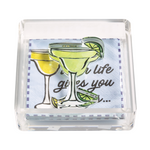 Clear acrylic napkin holder with light blue cocktail-themed napkins featuring a partial When life gives you quote and a bright green margarita glass decorative weight with a lime slice