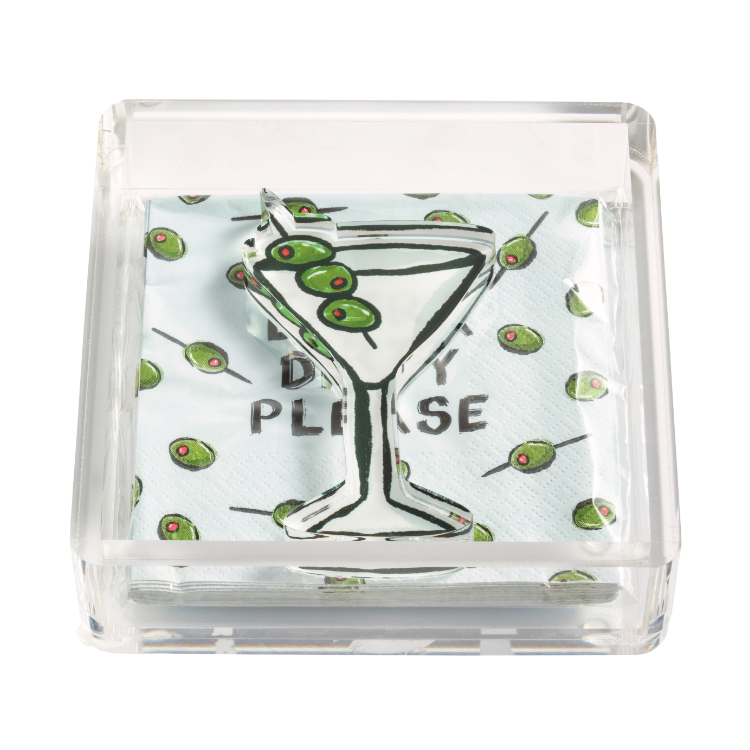 Clear acrylic napkin holder with light blue cocktail napkins patterned with green olives and the phrase 'DRY PLEASE' partially visible, topped by a clear acrylic martini glass cutout garnished with three green olives