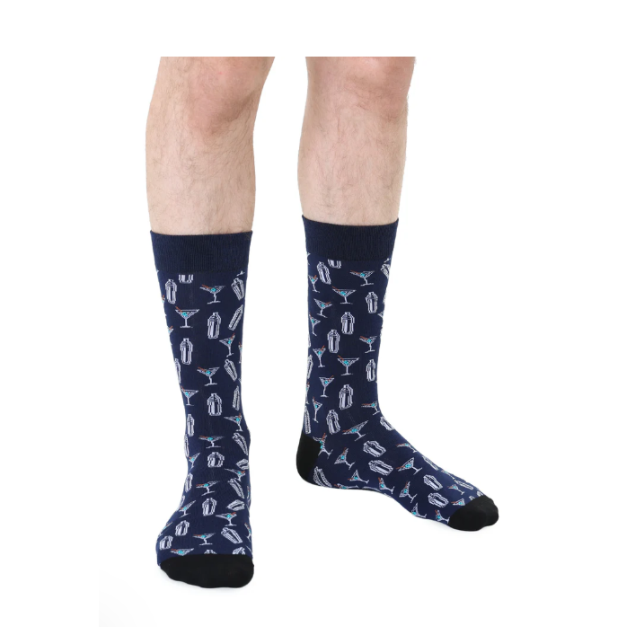 Photograph of a person wearing navy blue patterned crew socks featuring a repeated graphic of white cocktail shakers and martini glasses with turquoise and red accents and contrasting black heels and toes against a white studio background