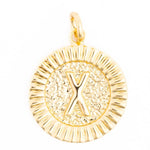 A polished gold circular charm features a raised letter X on a hammered background surrounded by a fluted border and a top hanging loop