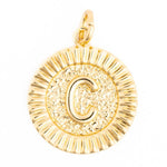 A circular gold initial C pendant featuring an embossed capital C on a textured background surrounded by a fluted outer border with a small attached bail