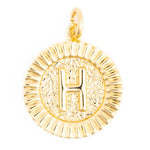 Gold circular pendant featuring a prominent embossed letter H against a hammered texture background and a fluted border