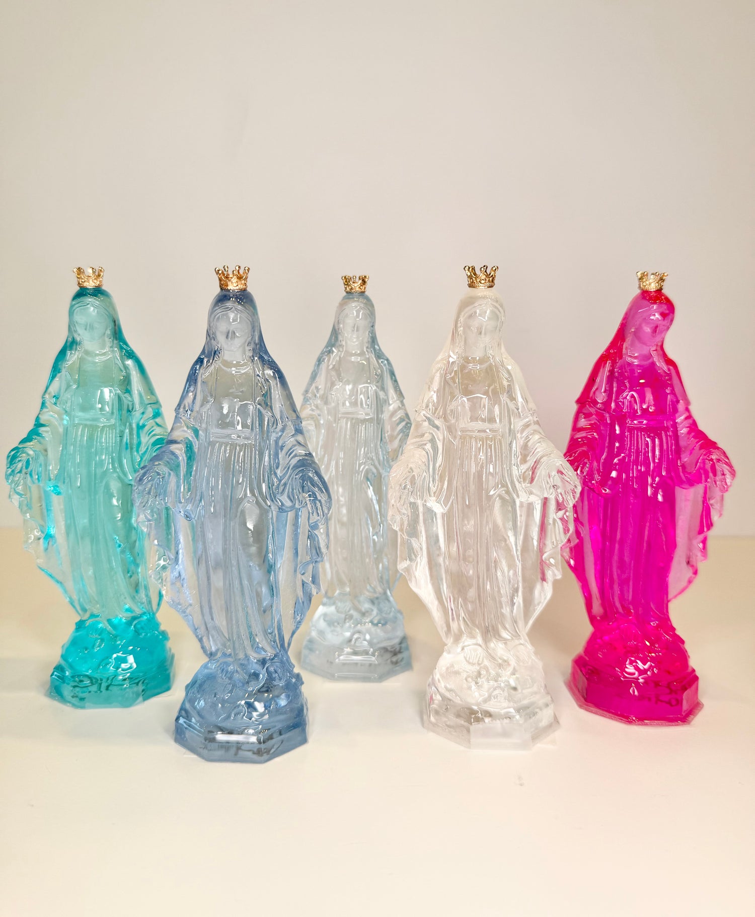Five translucent resin statues of the Virgin Mary in various colors with small gold crowns