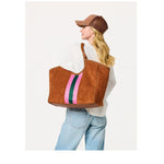 Person wearing a brown suede tote bag with pink and green stripes over the shoulder