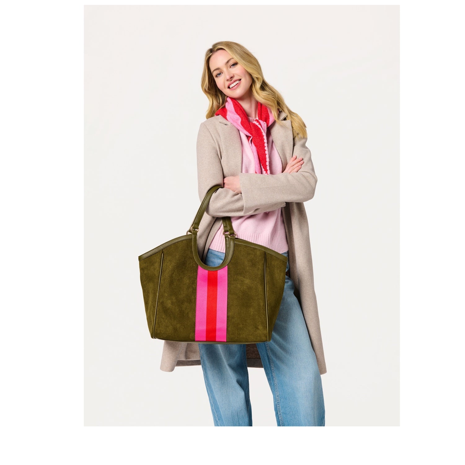 Woman wearing a beige coat and pink scarf holding an olive green suede tote bag with a pink and red center stripe