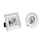 Two shiny silver photo frames with decorative wavy edges, one square displaying a black and white photo of a father holding a child, the other round showing a black and white photo of two laughing women
