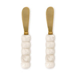 Gold-plated stainless steel and resin spreader knives featuring white marbled beaded handles and matte gold-tone blades set against a plain white background