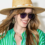Close-up portrait of a smiling woman wearing a straw hat with a white and orange beaded band dark sunglasses a vibrant green and blue striped shirt and gold butterfly earrings