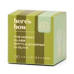 Product packaging by Here's How for The Moony Glass Bottle Stopper in Olive, featuring a two-toned olive green box with vertical stripes, a circular Modern Mixology TN USA seal, and 1.5 by 2.2 inch dimensions