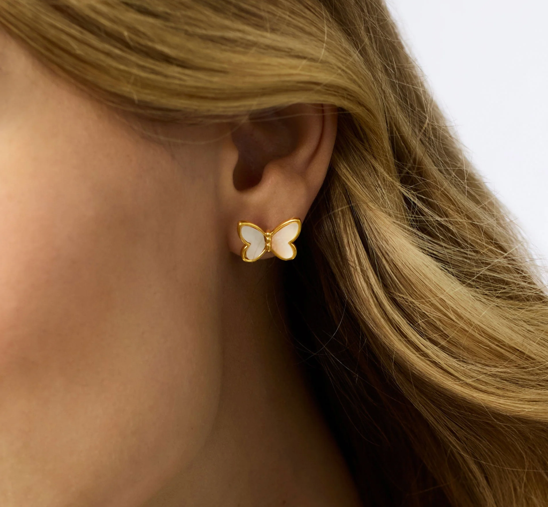 Gold butterfly stud earring with white inlay worn on earlobe
