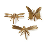 Three golden metallic insect sculptures featuring two detailed dragonflies with veined wings and one butterfly with ridged wings and antennae, arranged against a bright white background