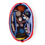 An overhead product shot of a red KUSSHI makeup bag unzipped on a white background, revealing a blue mesh interior organized with an orange beauty blender, a yellow detangling brush, and various cosmetic bottles