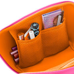 Vibrant pink and orange makeup bag open to reveal mesh pockets holding diverse cosmetics including a tropical patterned eyeshadow palette and a black lipstick with a blue heart design