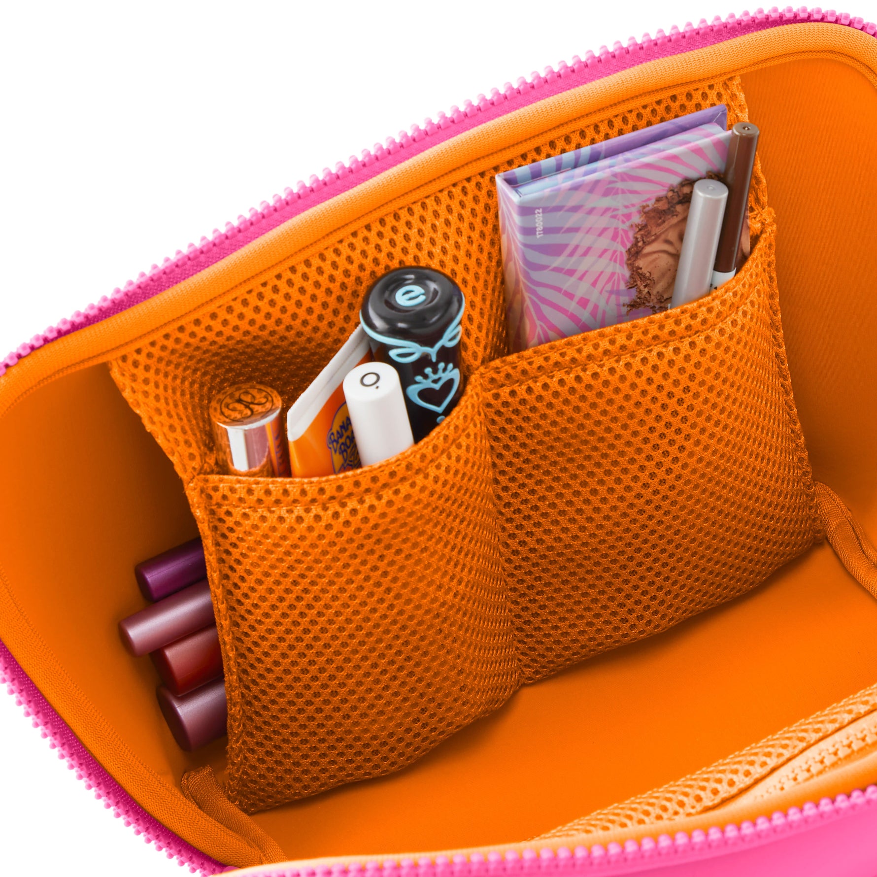 Vibrant pink and orange makeup bag open to reveal mesh pockets holding diverse cosmetics including a tropical patterned eyeshadow palette and a black lipstick with a blue heart design