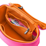 Open KUSSHI makeup organizer bag on a white background featuring a bright fuchsia pink exterior and vibrant orange interior with a mesh zippered pocket containing tweezers and a roller bottle
