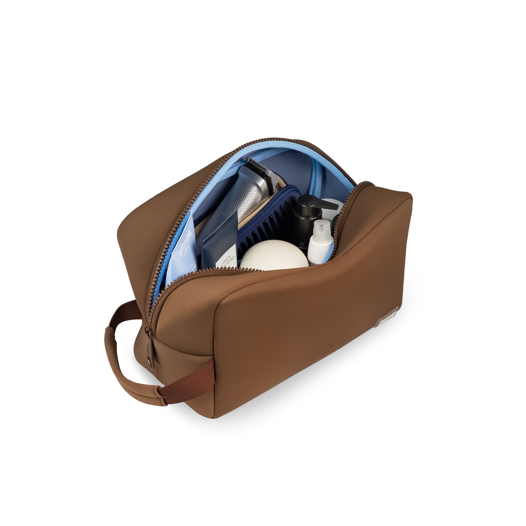 Product photography of an open brown toiletry bag with a light blue interior lining, revealing a silver electric shaver and dark blue comb against a white background