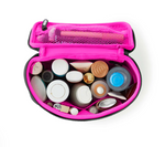 An overhead studio shot of a neon pink and black travel makeup bag unzipped, revealing various white, gold, and bronze cosmetic containers, a bottle with a bright blue cap, and makeup brushes in an internal mesh pocket