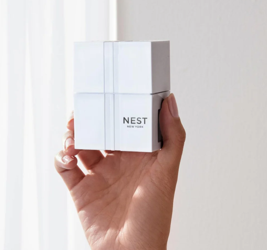 White Nest New York device with black branding and subtle vertical lines held in a hand against a bright softly lit background