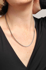 Close-up of a person's freckled neck and upper chest wearing a shiny silver box chain necklace over a black v-neck top