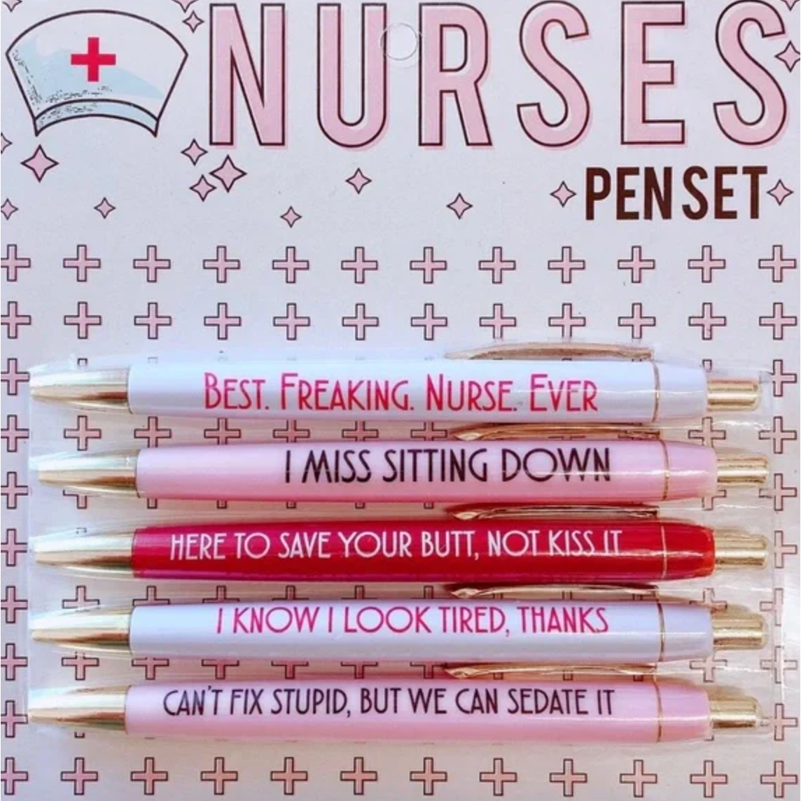 Product packaging of a five-piece Nurses Pen Set featuring white, pink, and red pens with gold accents, each inscribed with humorous phrases like BEST FREAKING NURSE EVER and CAN'T FIX STUPID BUT WE CAN SEDATE IT on a background patterned with pink crosses and a nurse's cap illustration