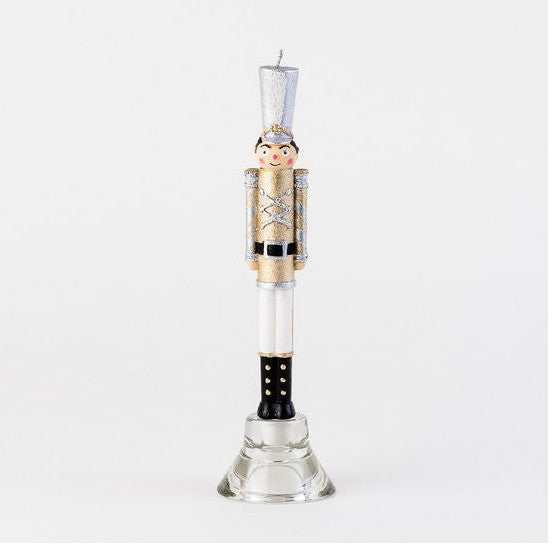 Nutcracker shaped taper candle in gold and silver uniform on a glass stand