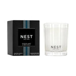 Nest New York Ocean Mist & Sea Salt scented candle in a black box with blue stripe details beside a clear textured glass vessel containing white wax