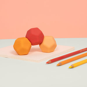 Three geometric shaped erasers and three colored pencils on a flat surface
